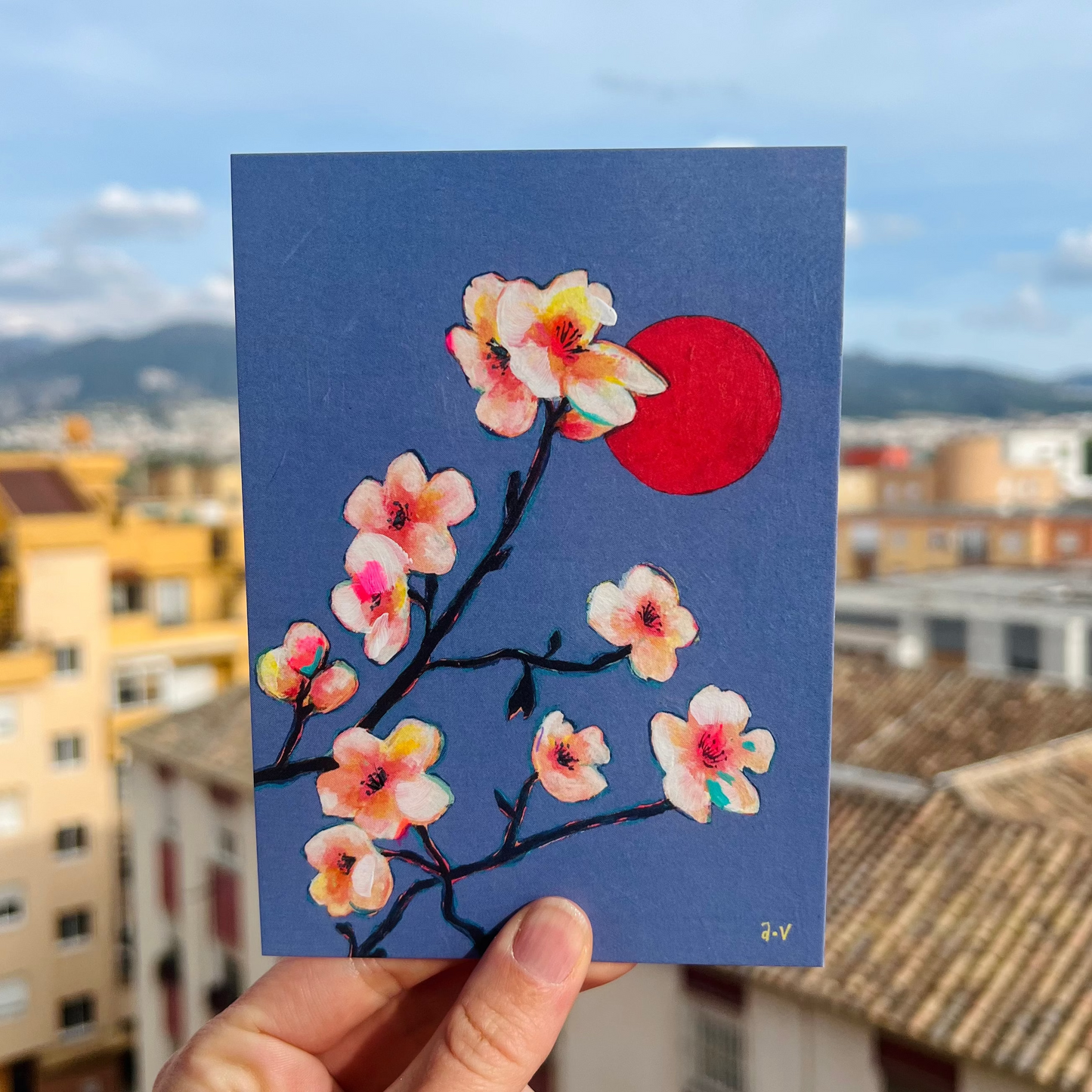 Card with almond blossom design held up against a cityscape